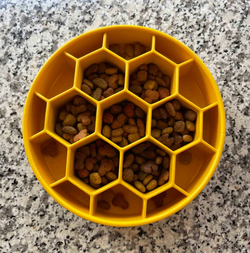 Yellow honeycomb-shaped pet feeder filled with dog food on a granite countertop