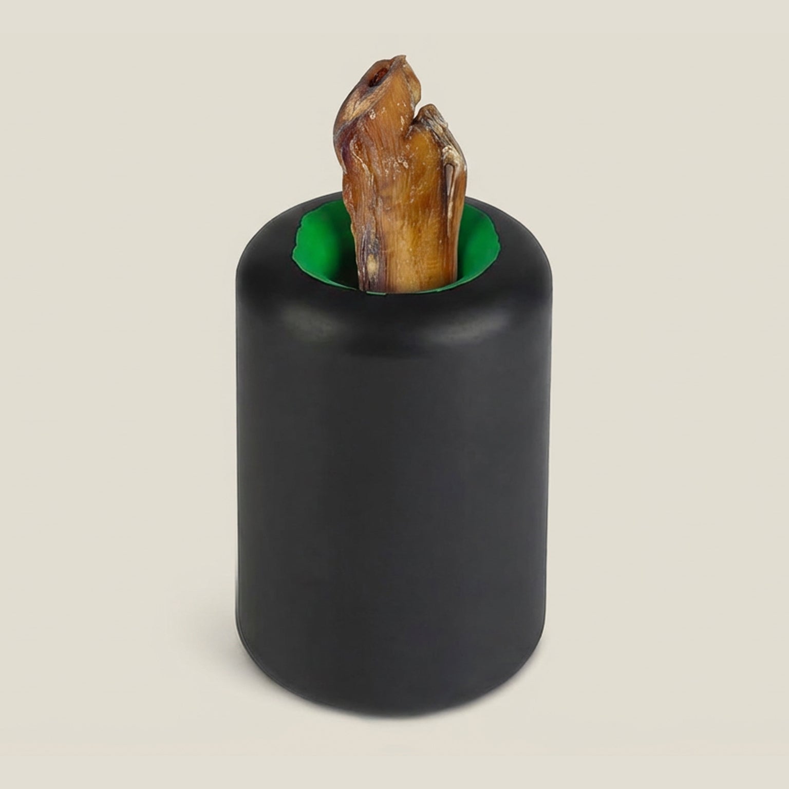 Black cylindrical rubber dog toy with a green interior holding a piece of beef bully stick inside on a beige background