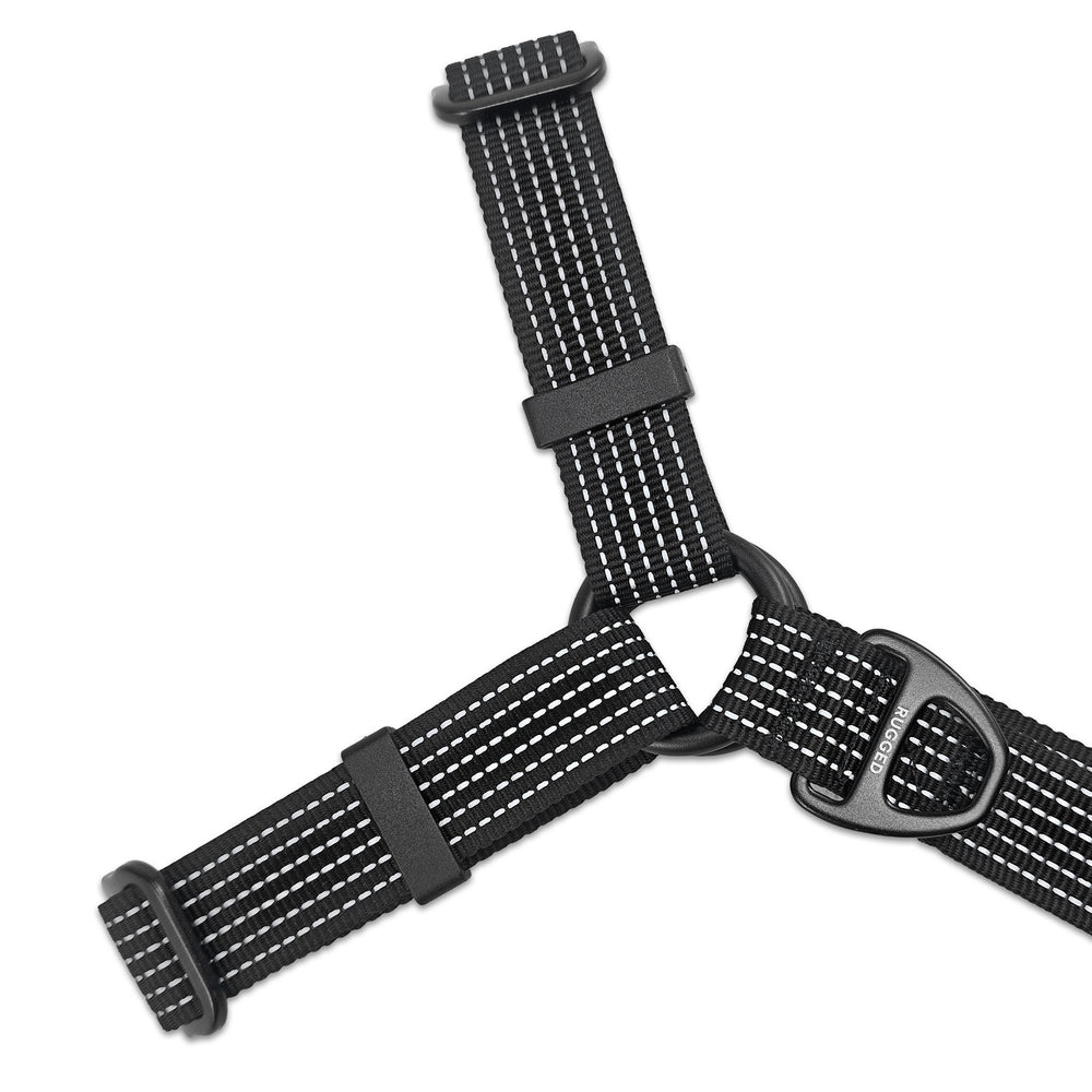 Close-up of black Rugged Dog Company no-pull harness showing reinforced metal O-ring junction connecting the Y-shaped reflective polyester webbing, branded aircraft-grade aluminum D-ring and adjustable hardware